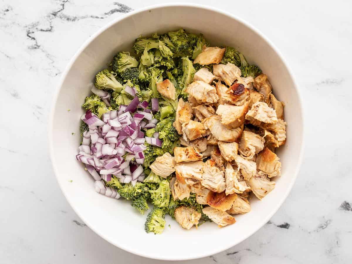 Broccoli, chicken, and red onion in a bowl.