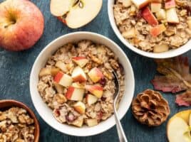 Two bowls of autumn fruit and nut oatmeal surrounded by apples, leaves, and pinecones