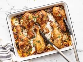 Oven roasted chicken drumsticks on a baking sheet with tongs