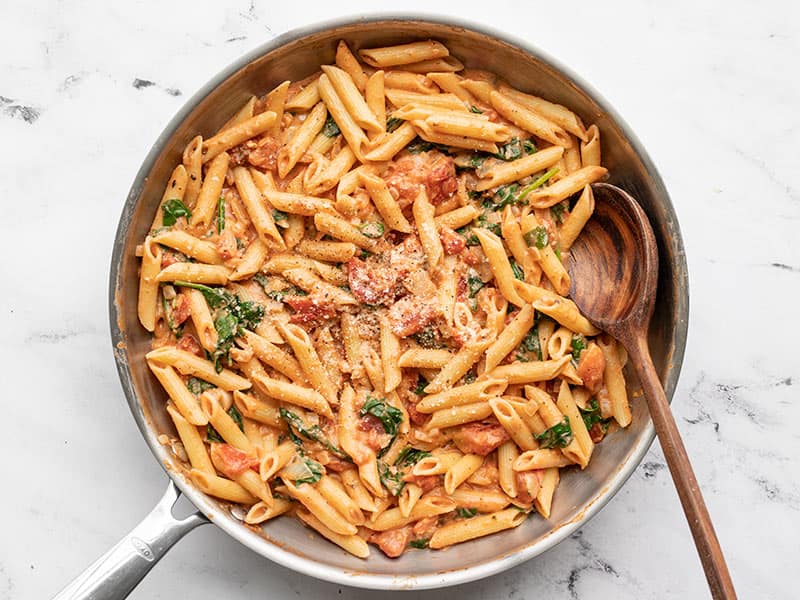 Finished creamy tomato and spinach pasta in the skillet with a wooden spoon