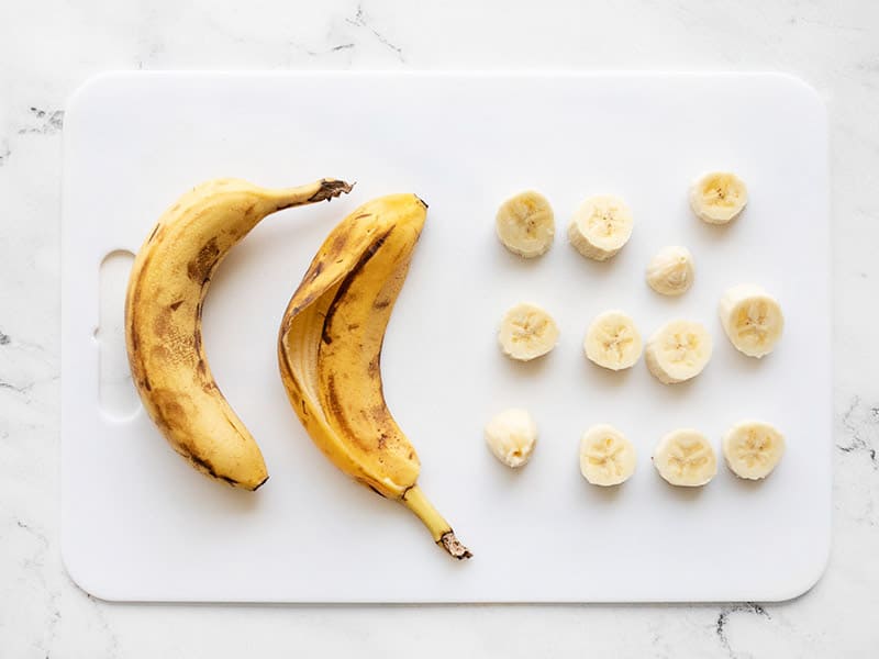 Sliced bananas on a cutting board next to banana peels