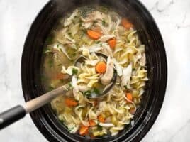 Overhead view of a ladle lifting chicken noodle soup out of the slow cooker
