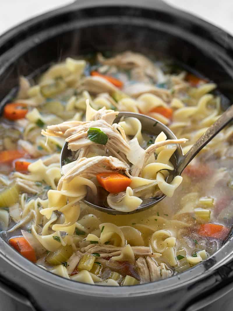 Front view of a ladle lifting some chicken noodle soup out of the slow cooker